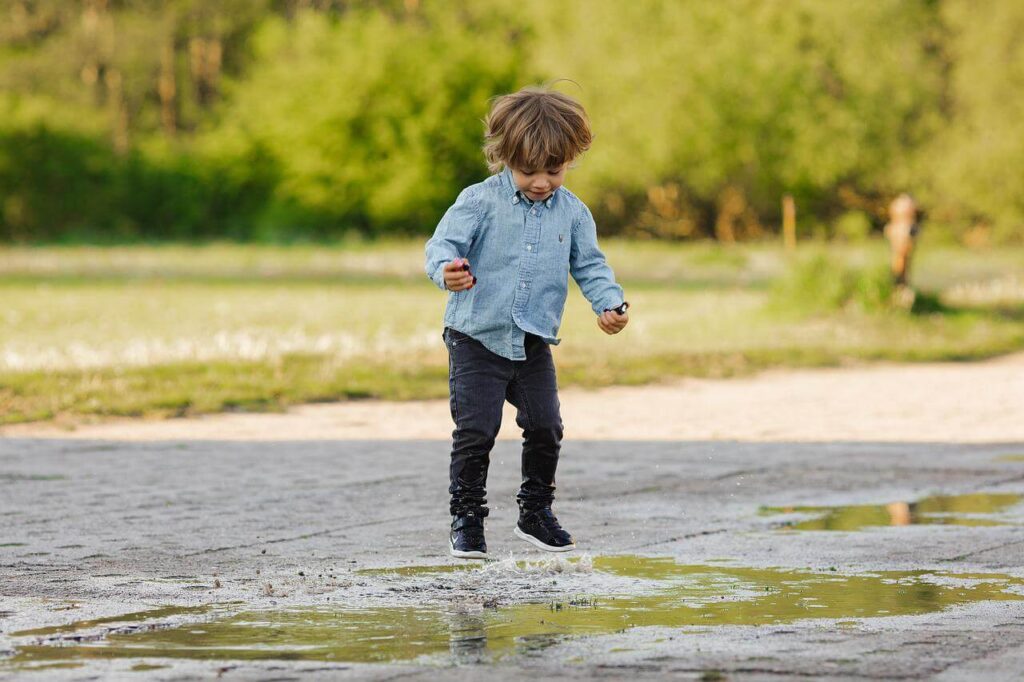 A young boy is jumping in a puddle in the park.